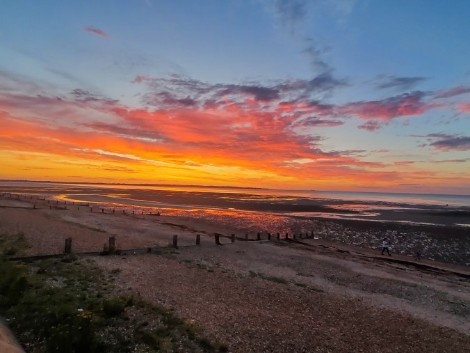 shingle beach in foreground, blue sky streaked with yellow and pink
